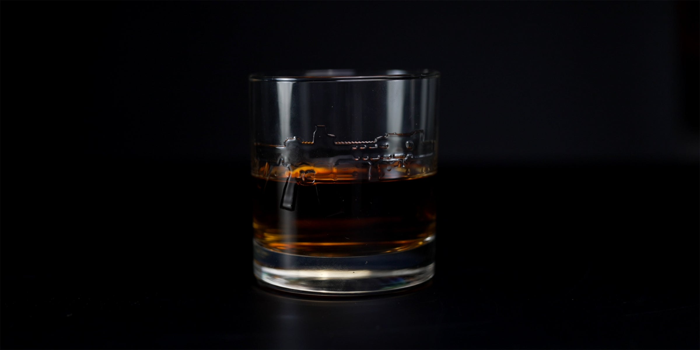 rocks glass embossed with an AR15 rifle, half full with bourbon. black background.