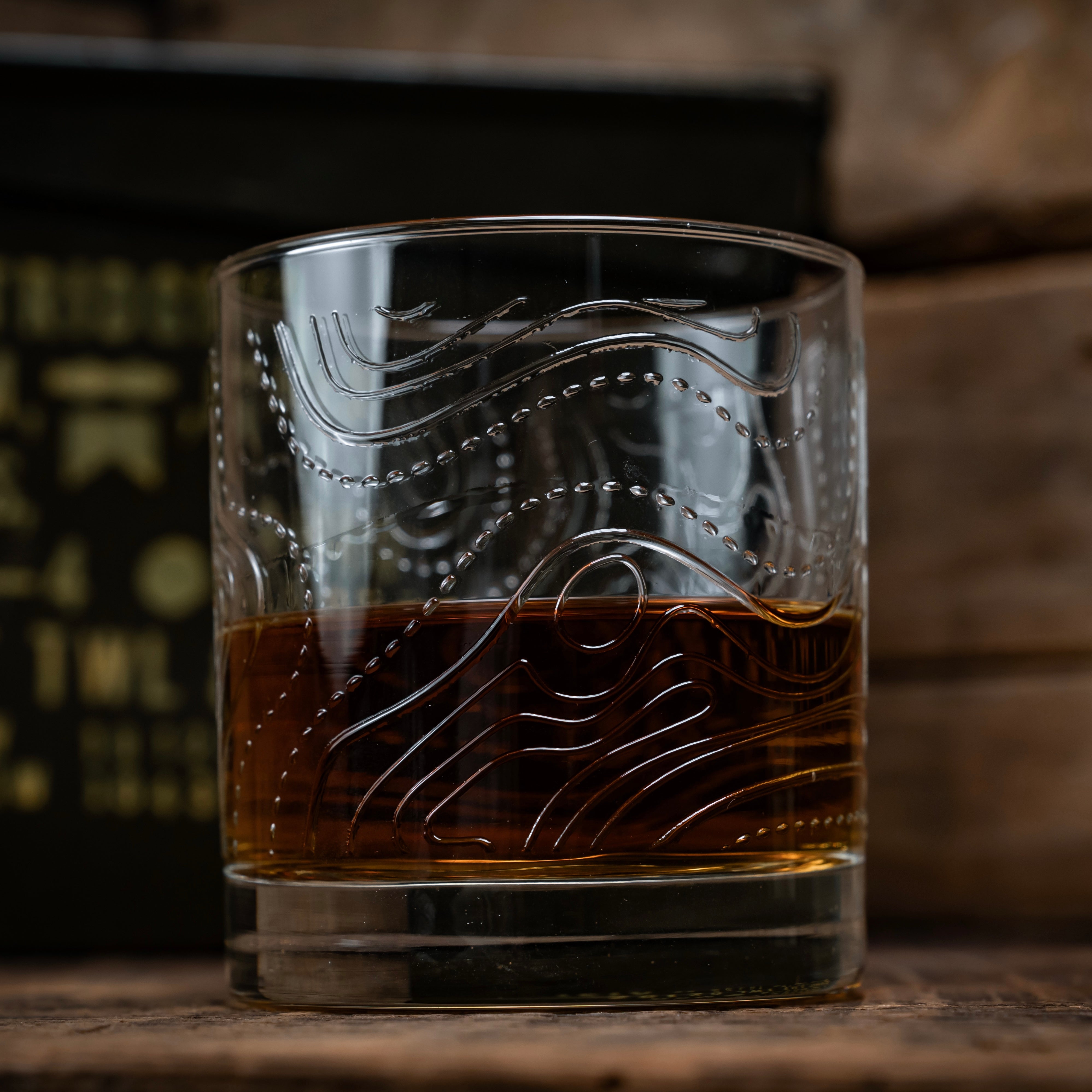 whiskey glass with topographic map lines embossed, glass half full with bourbon