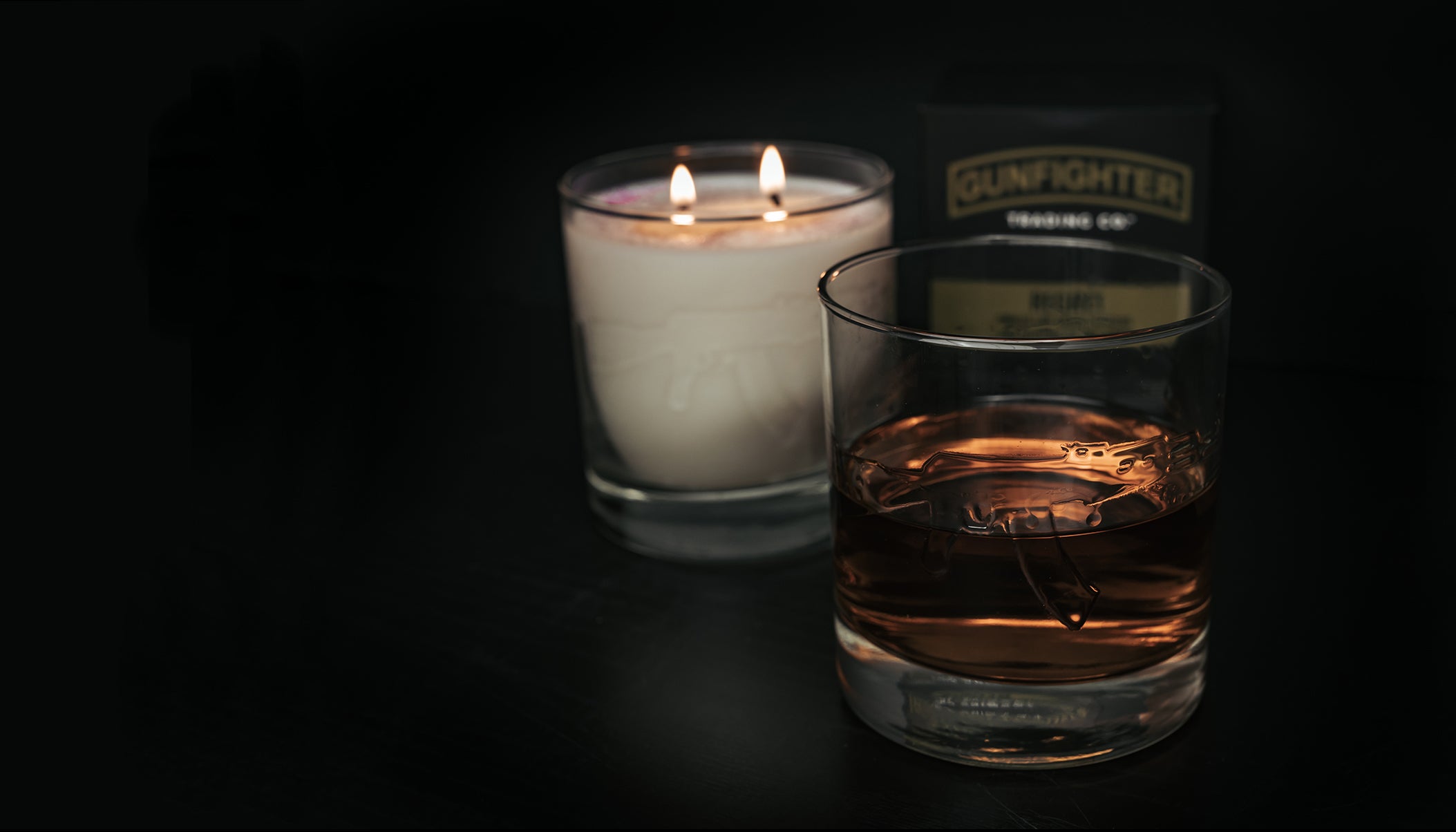 Rocks glass with embossed AK47 half full of bourbon, lit bourbon glass candle, and packaging box